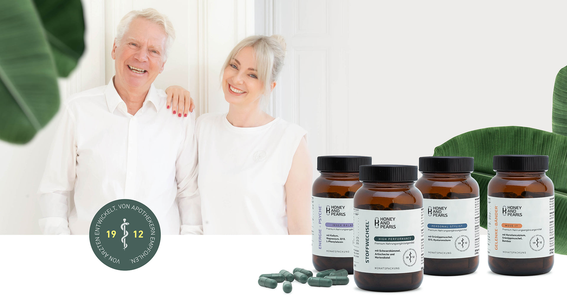 Dr. Volkher Zähres und Carina Weihgold in weiß gekleidet, Carina legt Hand auf die Schulter von Dr. Volkher, ihrem Vater. Am unteren Bereich des Bildes ist ein rundes Siegel zu sehen: 1912, Von Ärzten entwickelt, von Apotekern empfohlen. Im Vordergrund sind Honey and Pearls Dosen: Inner Balance, High Performance, Personal Stylist, Move It. Banenenblätter sind dezent und dekorativ sichtbar und geben ein natürliches Gefühl.