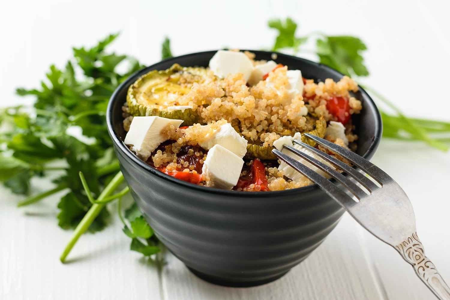 Proteinreiche Gemüsepfanne mit Quinoa, Tofu und Zucchini in einer schwarzen Schale, angerichtet mit frischen Kräutern – leichtes Sommergericht.
